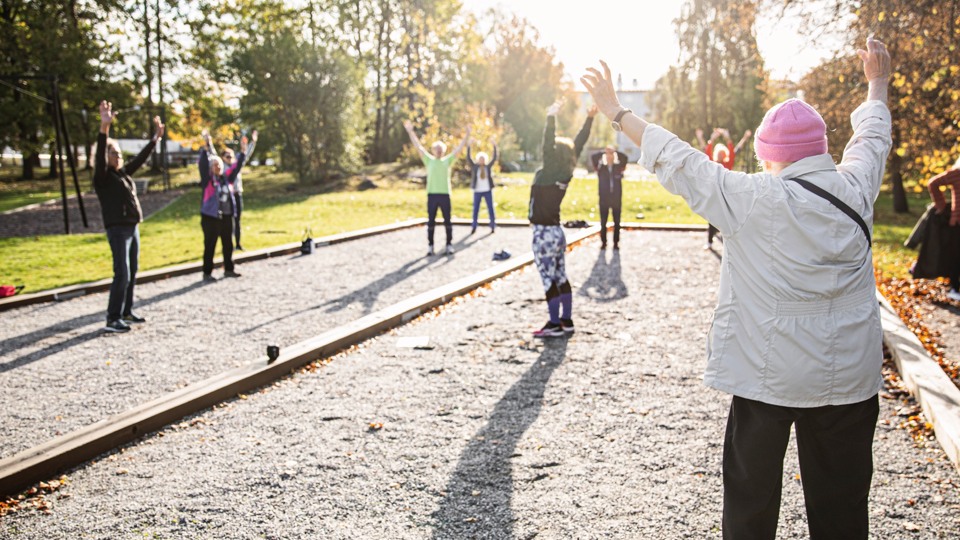 Några seniorer som gympar i solskenet vid en boulebana.